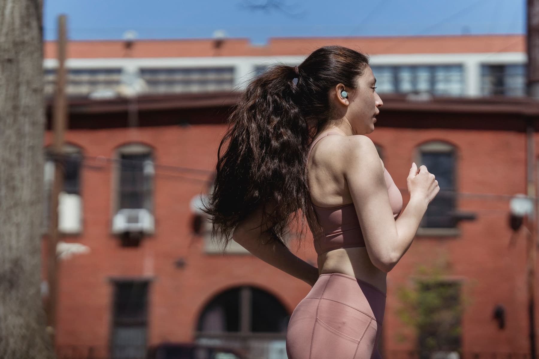 A runner in an urban setting wearing open-ear sport headphones on a sunny day