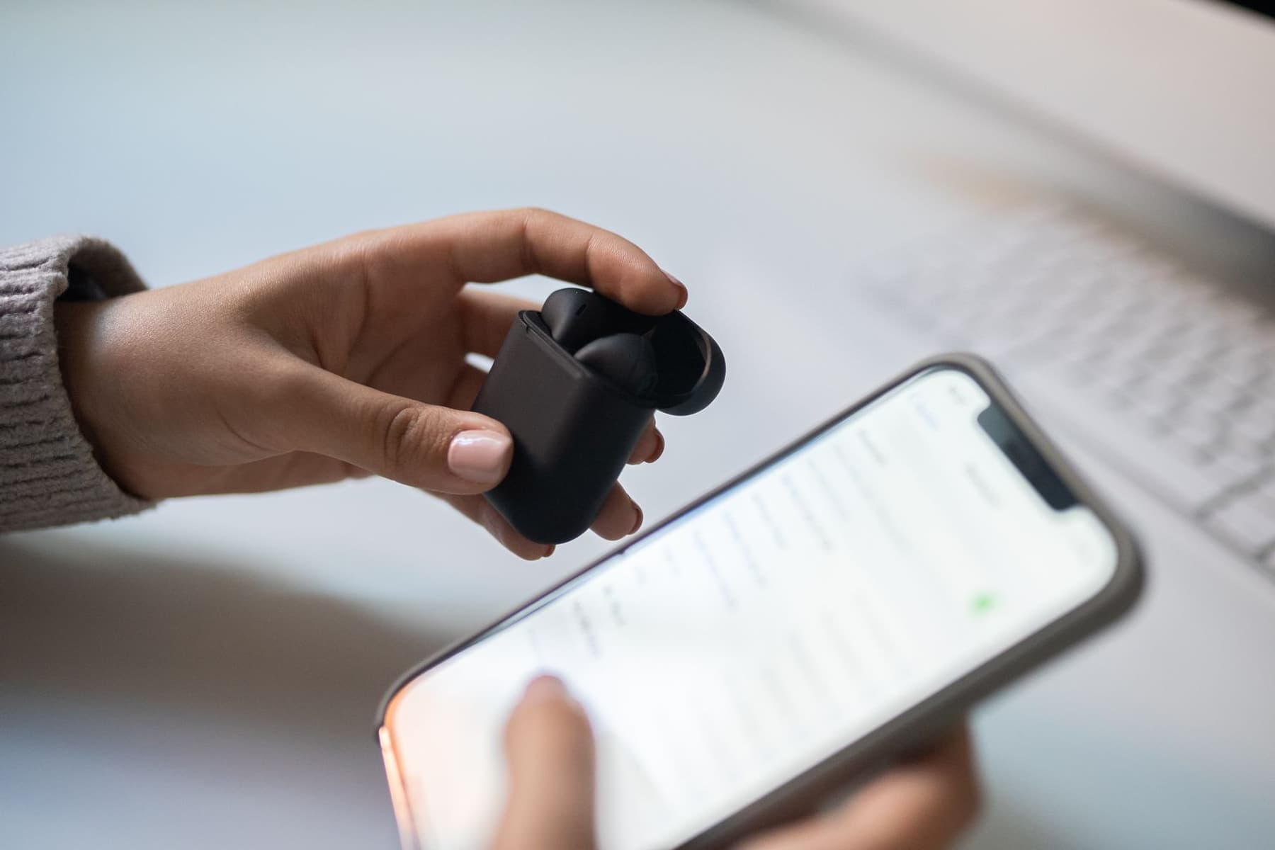 A pair of hands connecting wireless earbuds to a smartphone