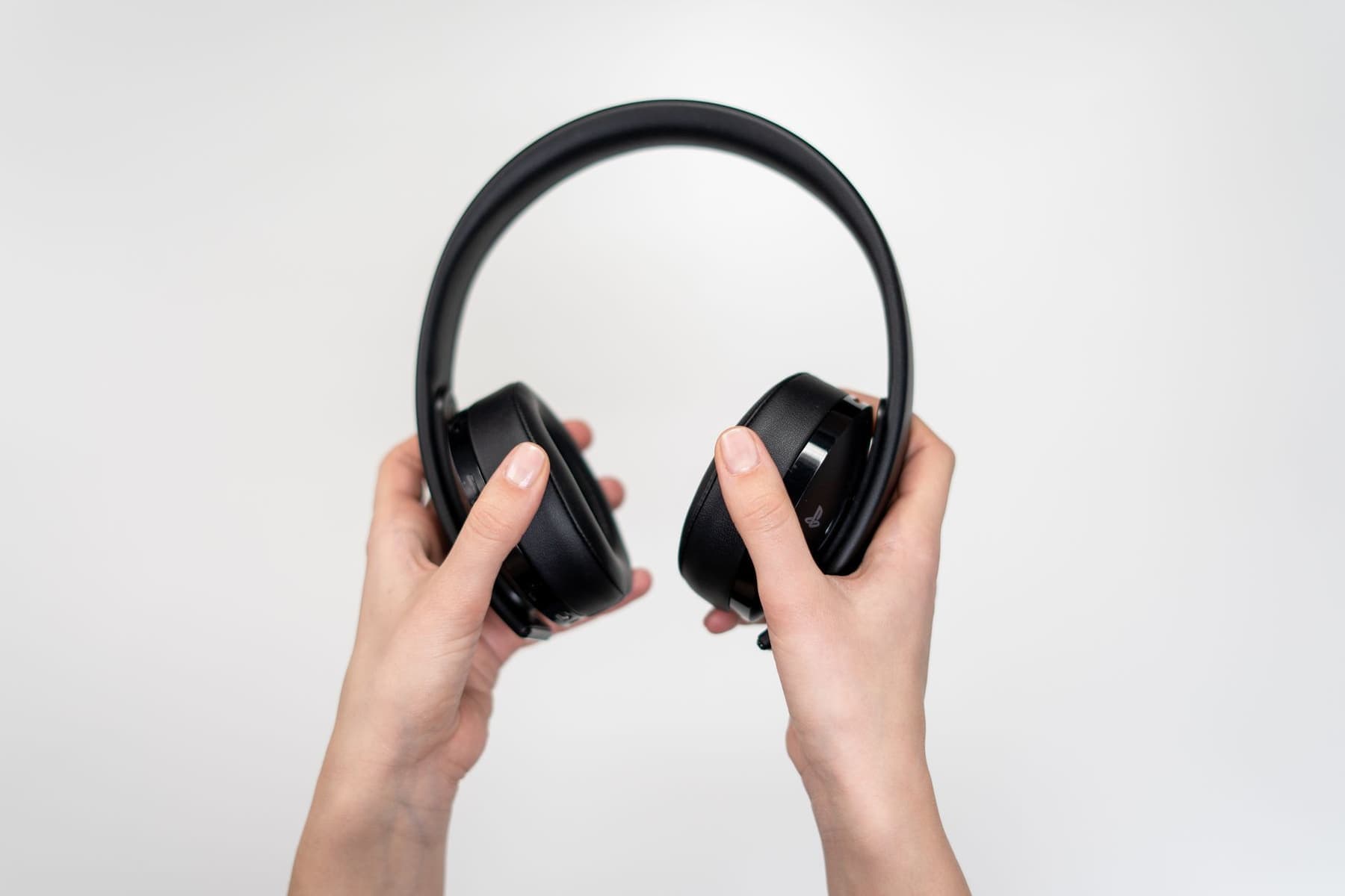 A pair of hands holding black wireless headphones