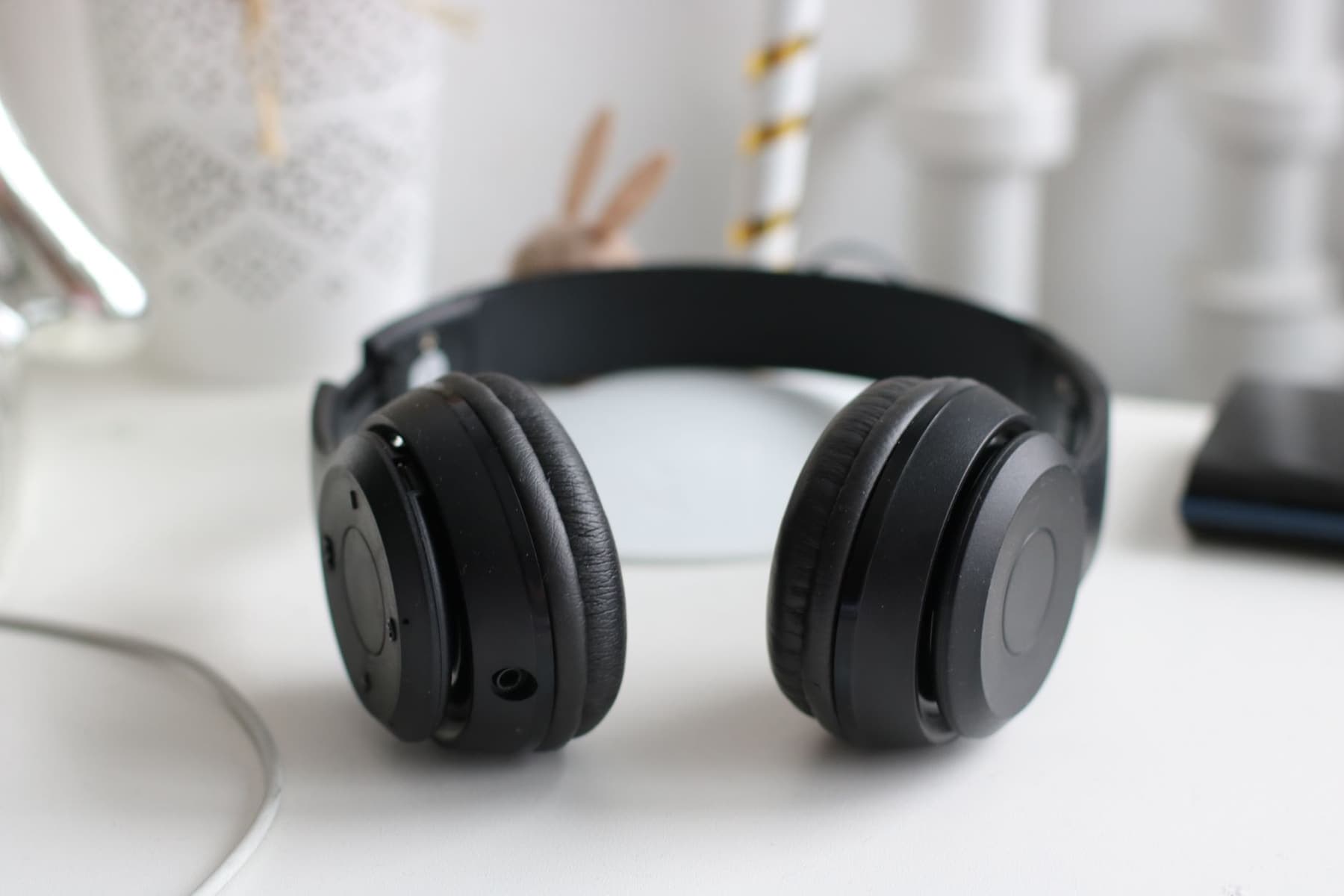A well-used pair of black wireless headphones resting on a white desk