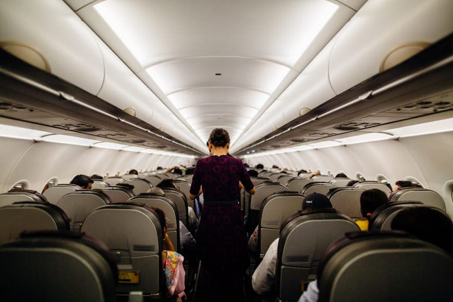 Interior view of an airplane cabin with passengers seated and a flight attendant in the aisle