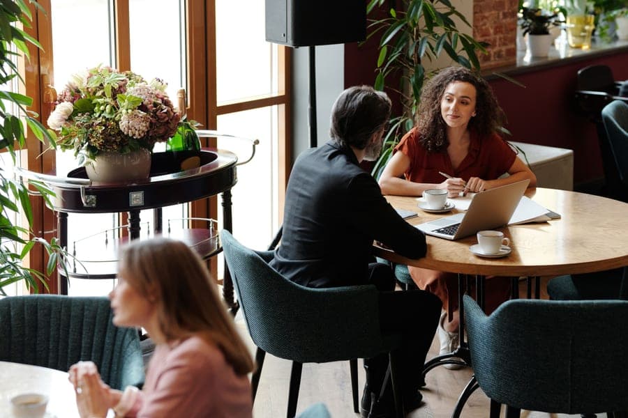 Two people talking over laptops in a busy cafe