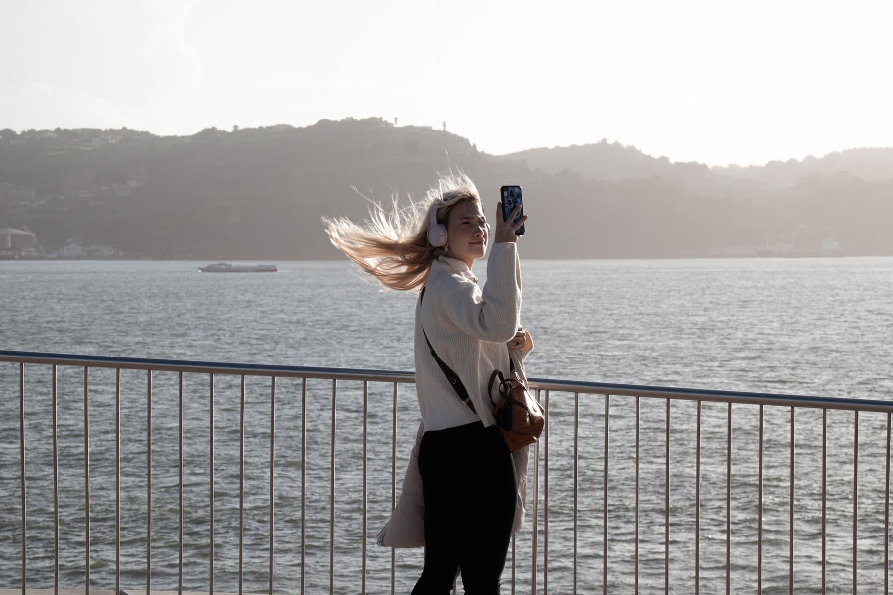 A woman wearing headphones on a windy waterfront