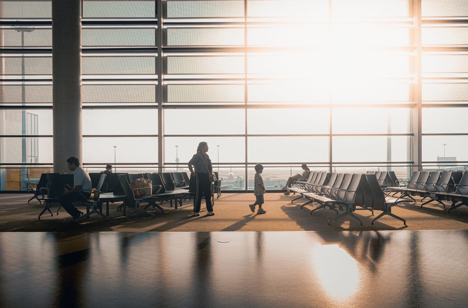 Silhouettes of travelers in a sunlit airport terminal