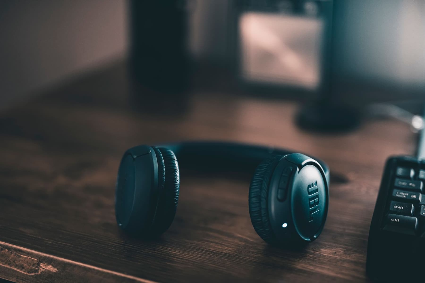 A pair of wireless over-ear headphones on a wooden desk in low light