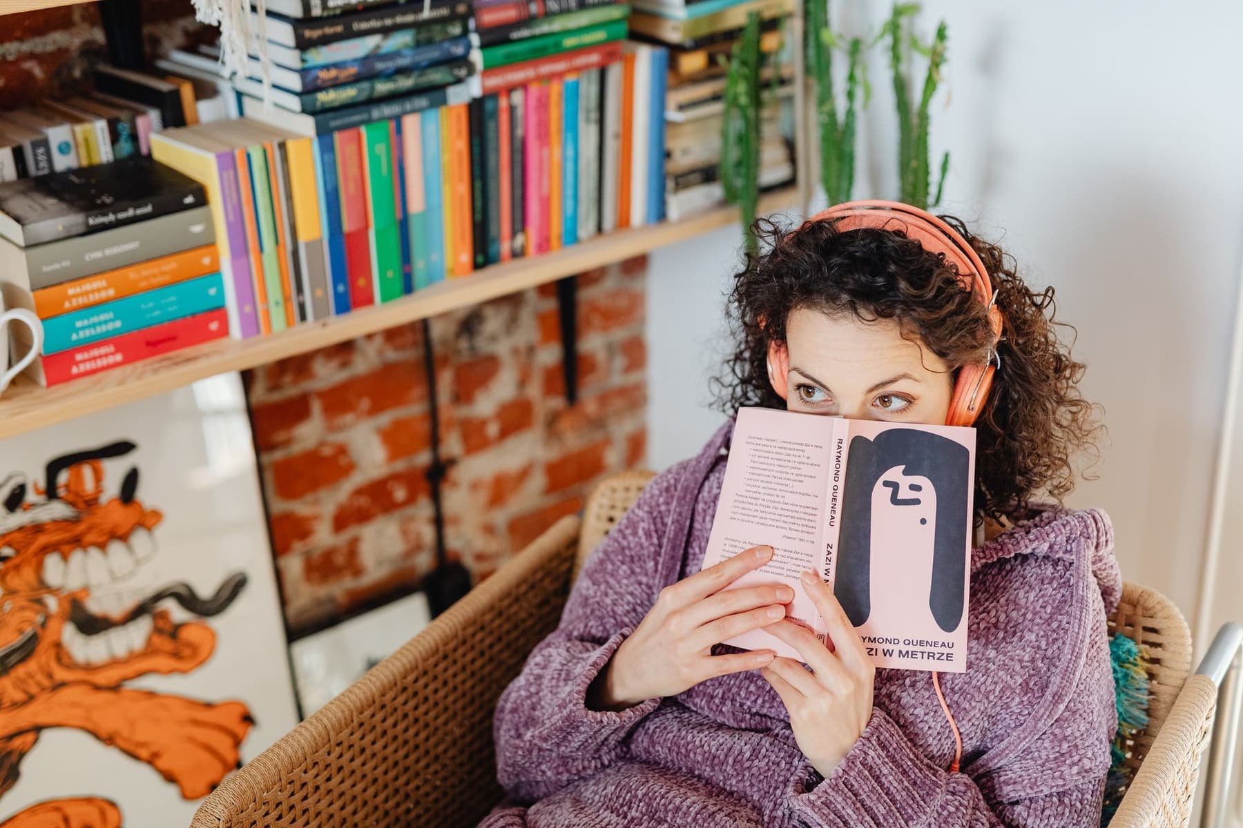 A person in a knitted sweater reading a book while wearing headphones