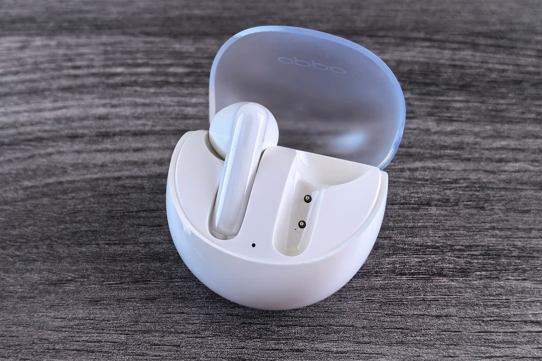 A pair of white wireless earbuds beside an open charging case on a wooden surface