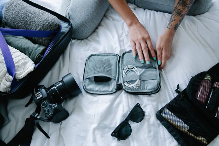 Traveler packing electronics, camera and sunglasses into a suitcase