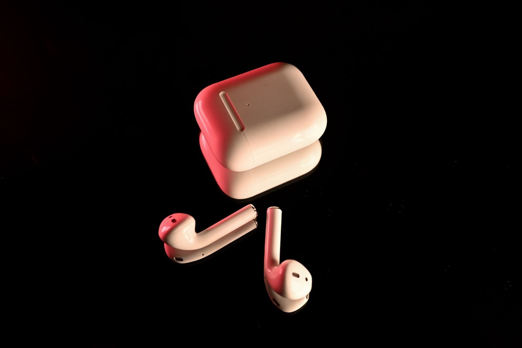 White wireless earbuds beside their charging case on a dark reflective surface