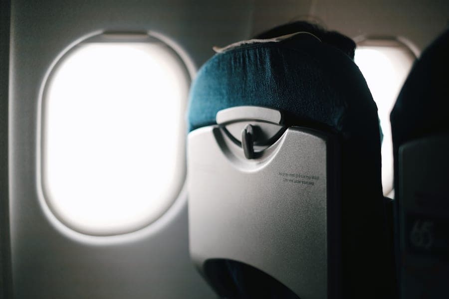 An airplane seat beside a window with bright sky outside