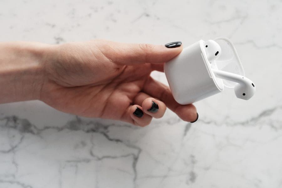 A hand holding wireless earbuds against a marble background