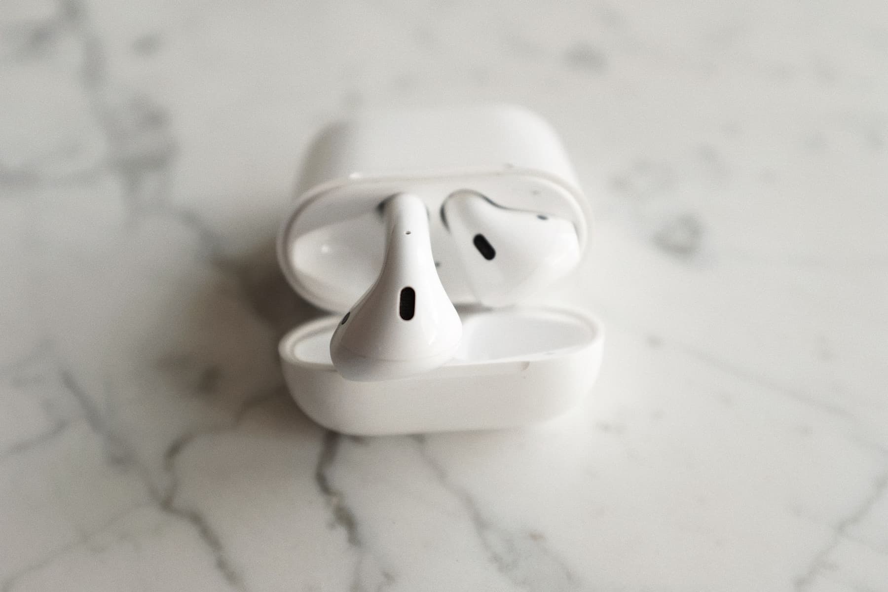 Two wireless earbud charging cases side by side on a marble surface