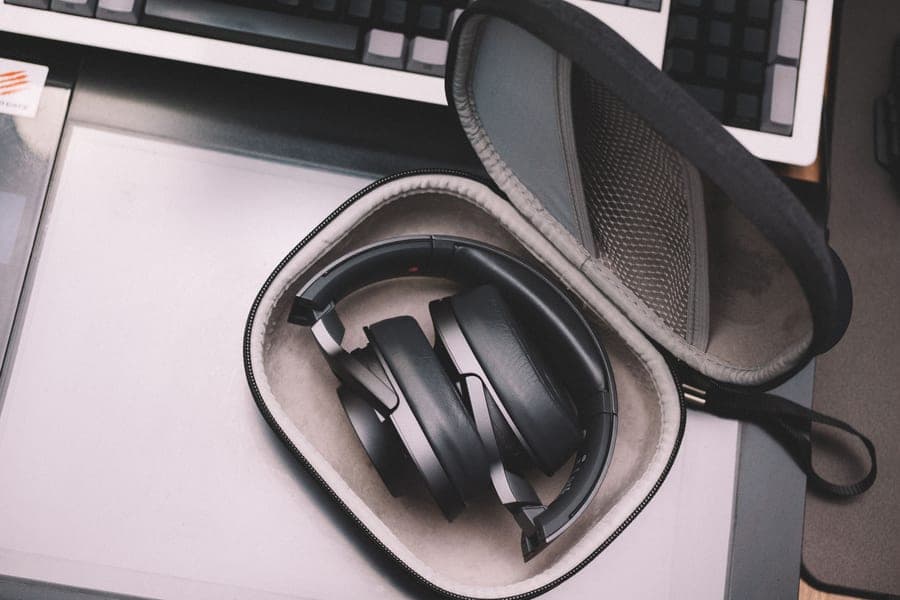 Compact black wireless headphones stored in a protective case on a desk