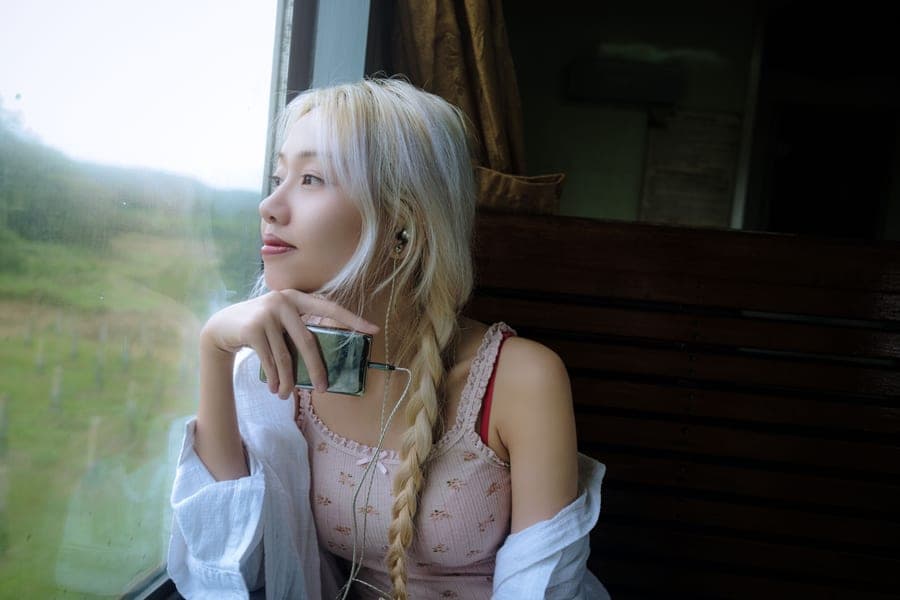 A woman wearing headphones on a train looking out at a green landscape