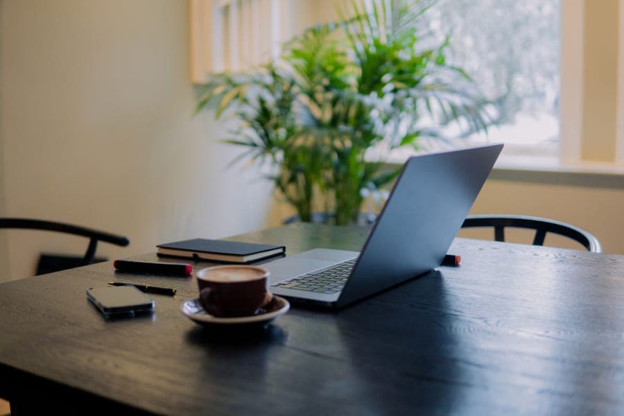 A warm home workspace with a laptop, coffee and a potted plant