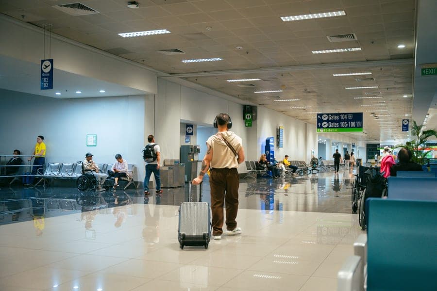 Passengers in a spacious airport terminal, some seated and others walking