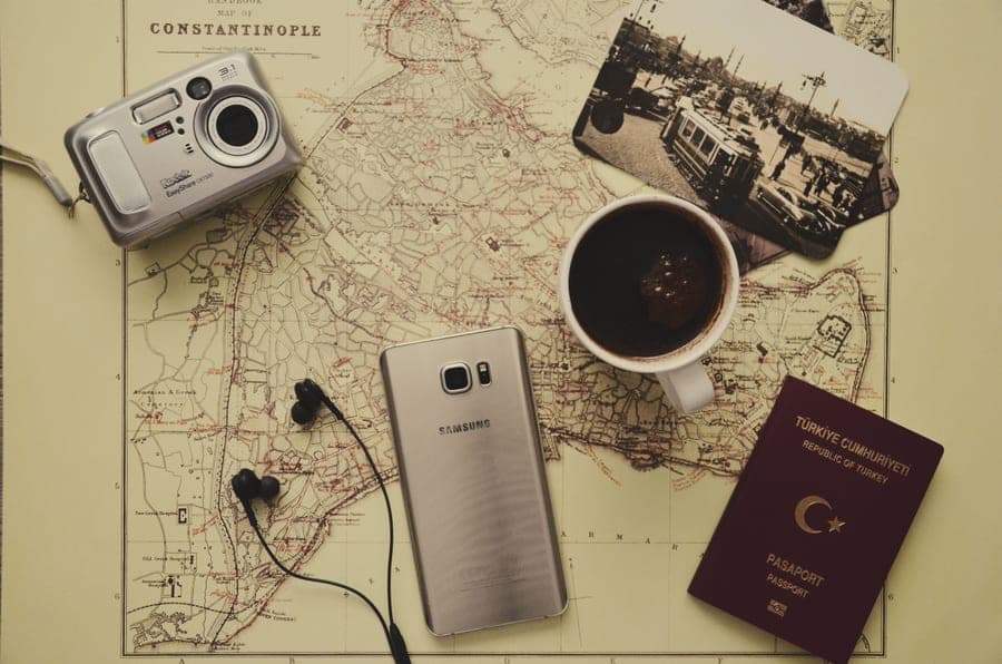Flat lay of travel essentials including a map, passport, coffee and gadgets on a desk