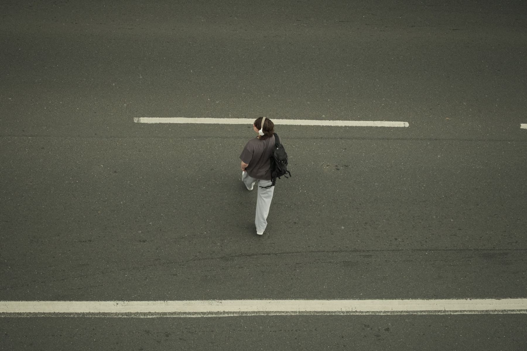 A single person walking along a wide city road seen from above